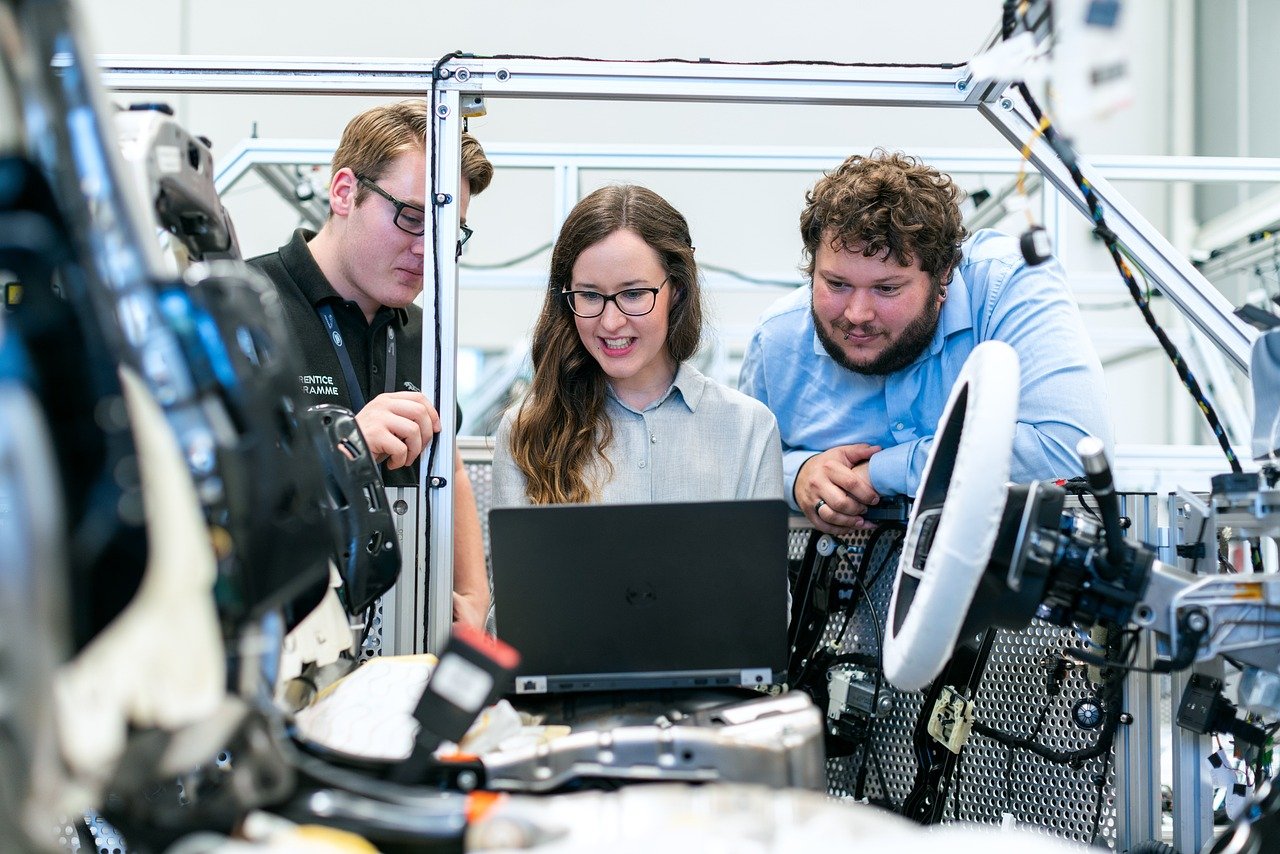 Three engineers reviewing work on a laptop beside automated machinery in a workshop