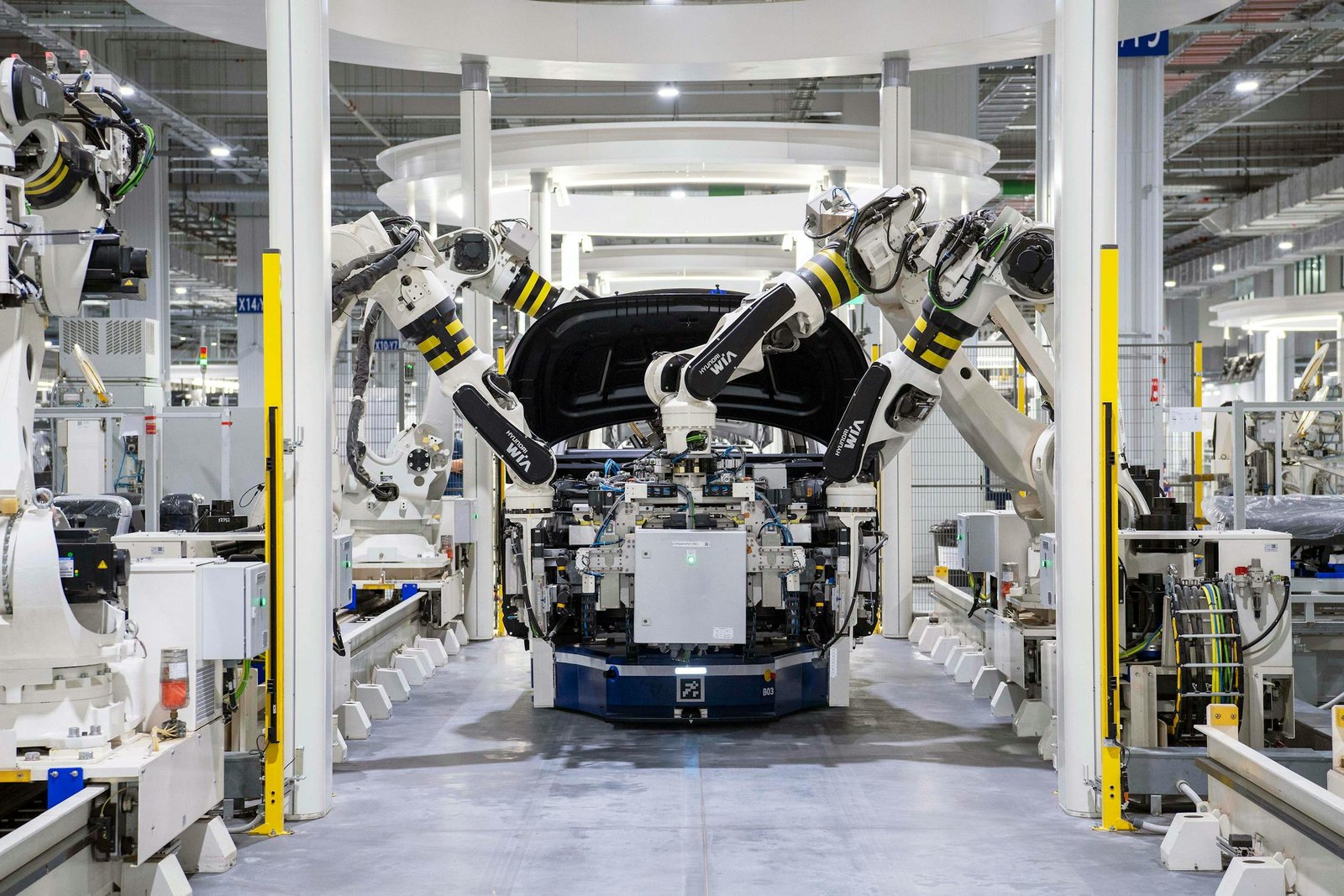 Multiple white robot arms assembling a car on a factory production line