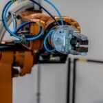 Orange industrial robot arm with a metal gripper on a factory floor