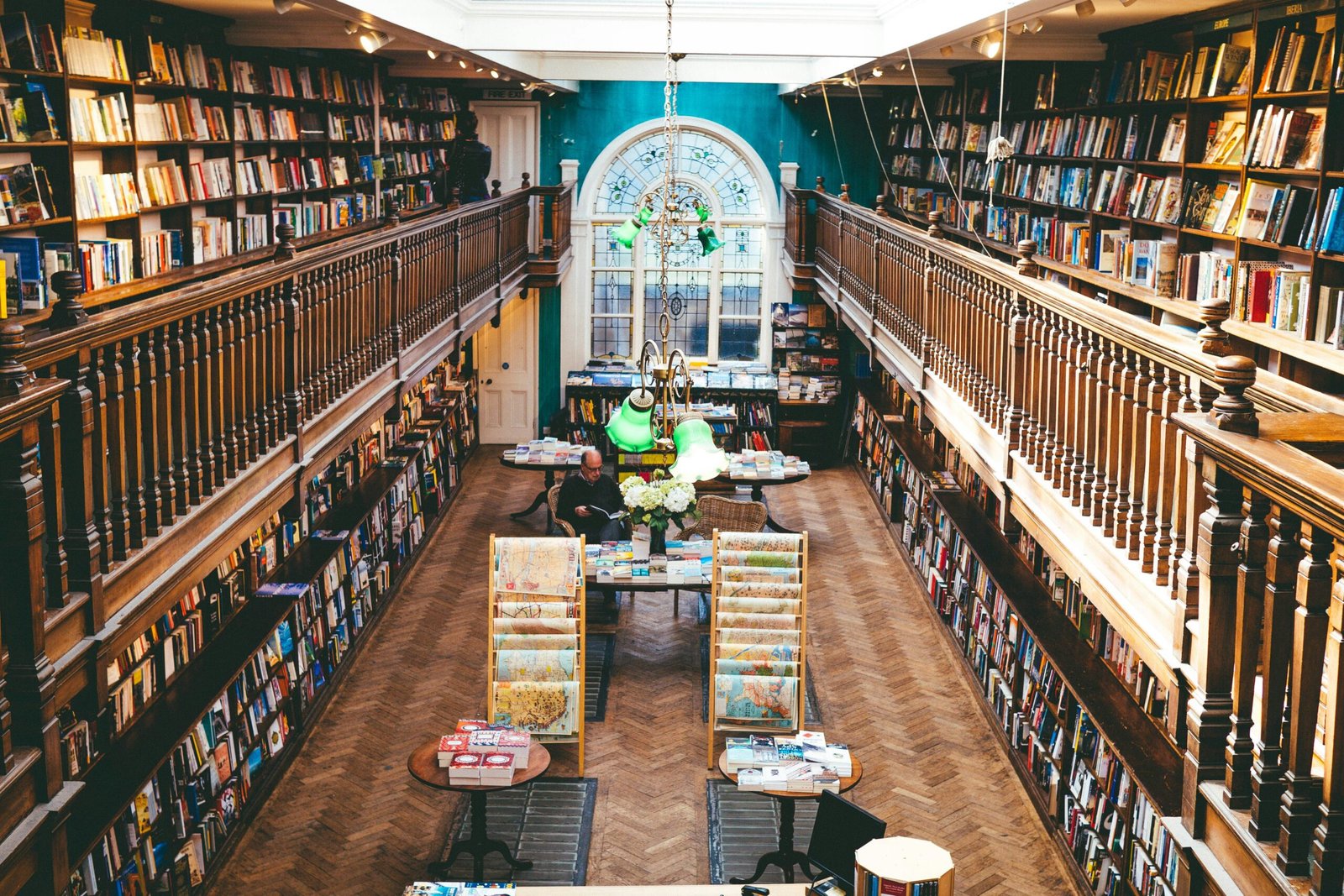 Two-storey library with wooden bookshelves full of books and a person reading at a table below