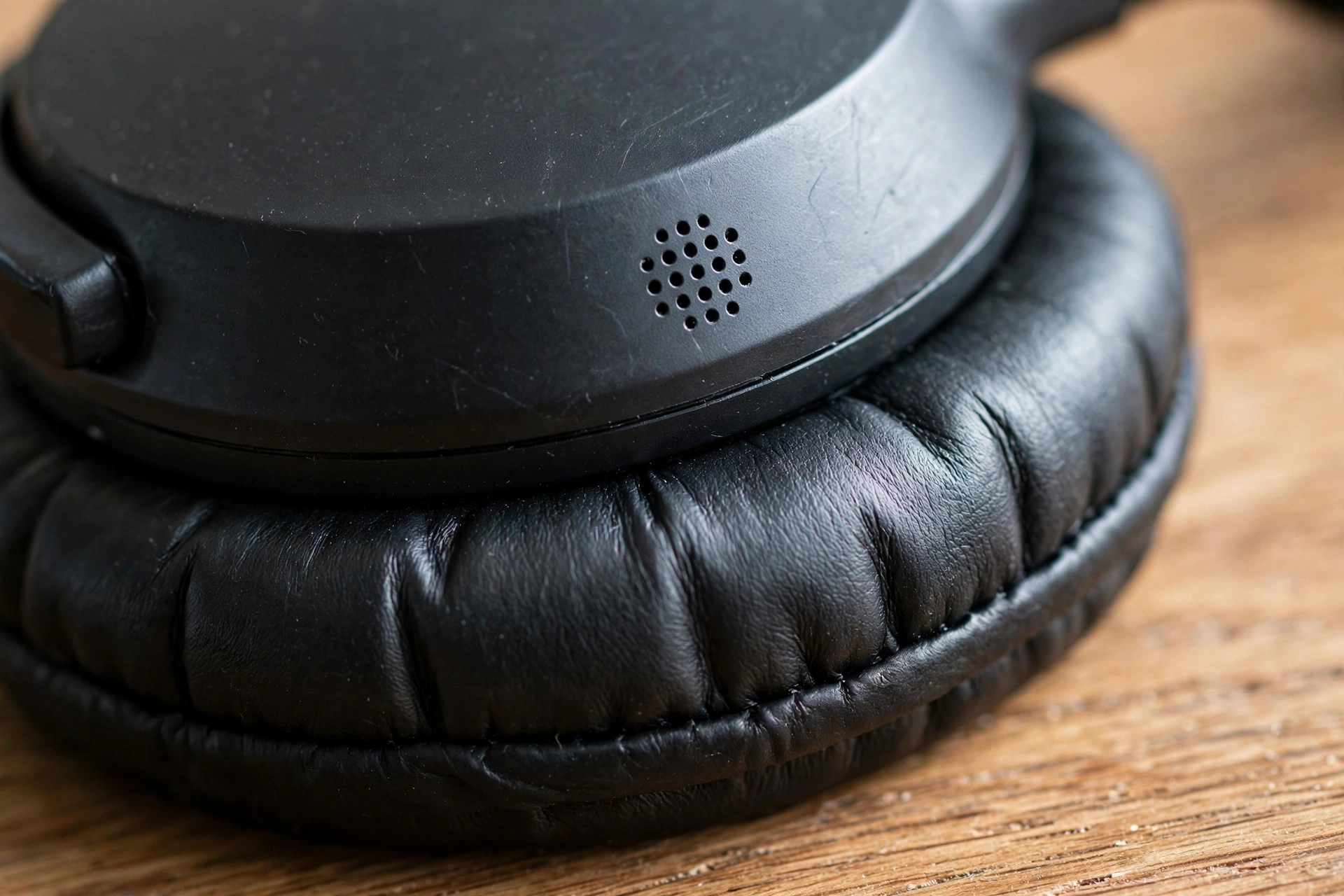 Close-up of a headphone earcup showing its microphone holes and soft ear cushion